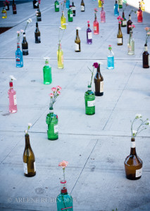 Colorful bottles holding flowers aligned on sidewalk